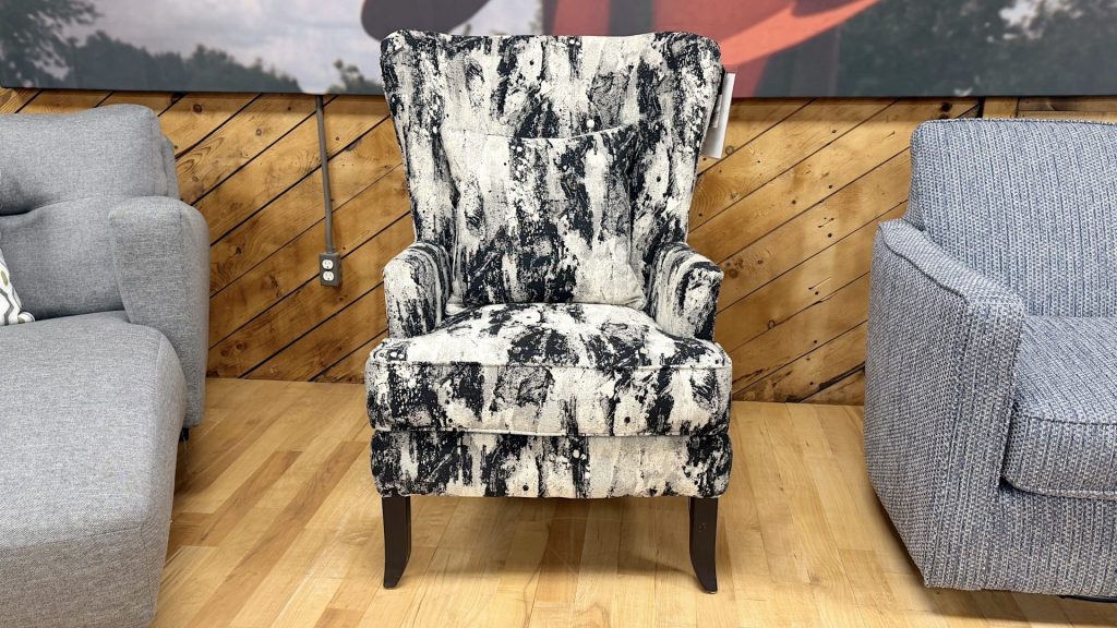 High-back wingback accent chair with a bold, abstract black and white textured pattern, including a matching throw pillow, displayed on a light wood floor at a furniture store.