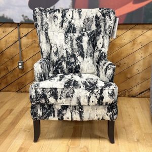 High-back wingback accent chair with a bold, abstract black and white textured pattern, including a matching throw pillow, displayed on a light wood floor at a furniture store.