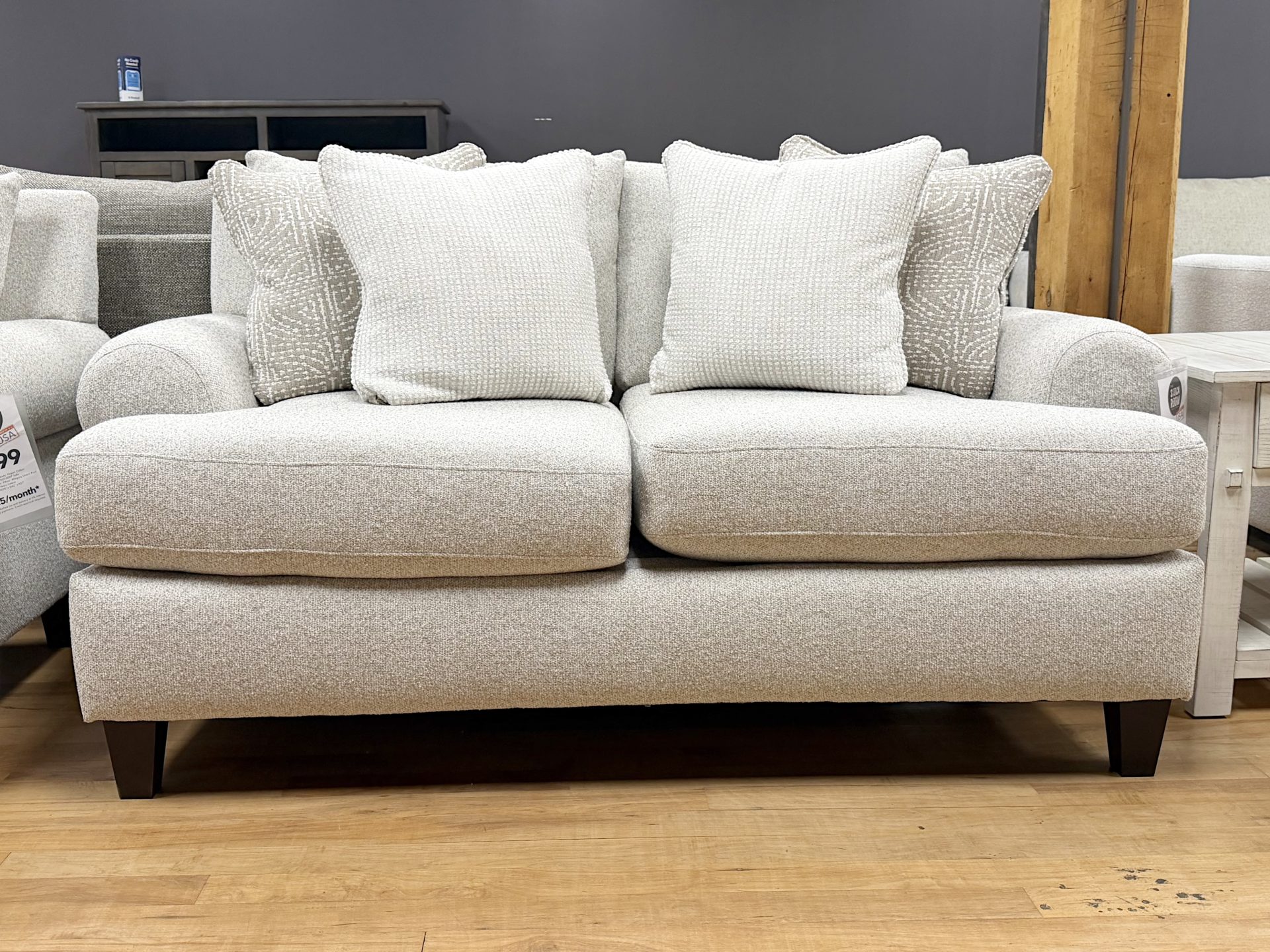 Tezza-0881 A contemporary light beige upholstered loveseat decorated with textured white and tan accent pillows.