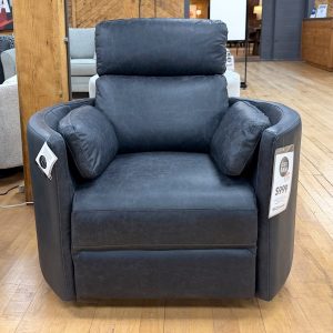 Modern charcoal grey faux-leather recliner chair with built-in side bolster pillows, displayed on a light hardwood showroom floor at The Stock Room.