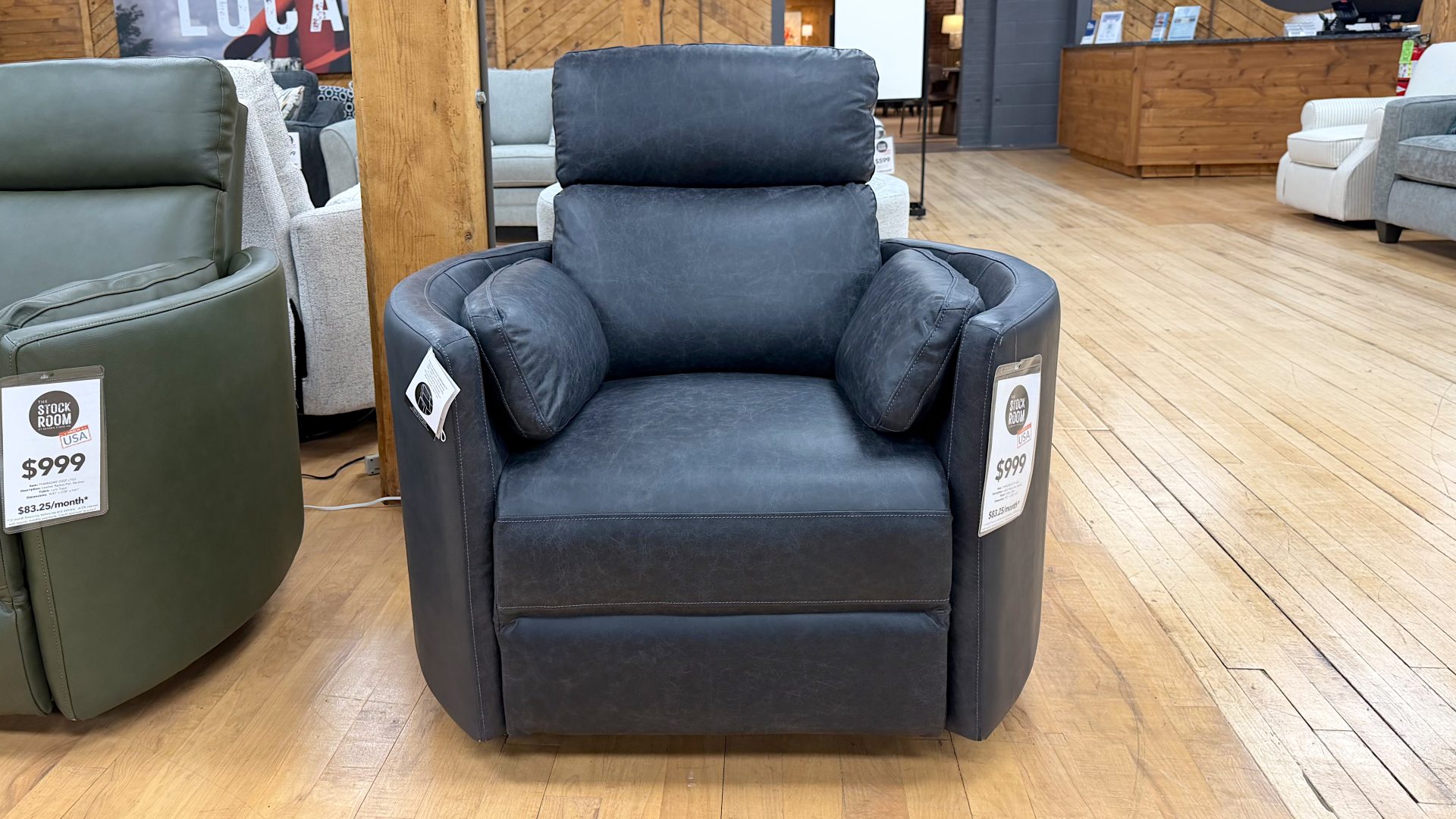 Tezza-2347 Modern charcoal grey faux-leather recliner chair with built-in side bolster pillows, displayed on a light hardwood showroom floor at The Stock Room.