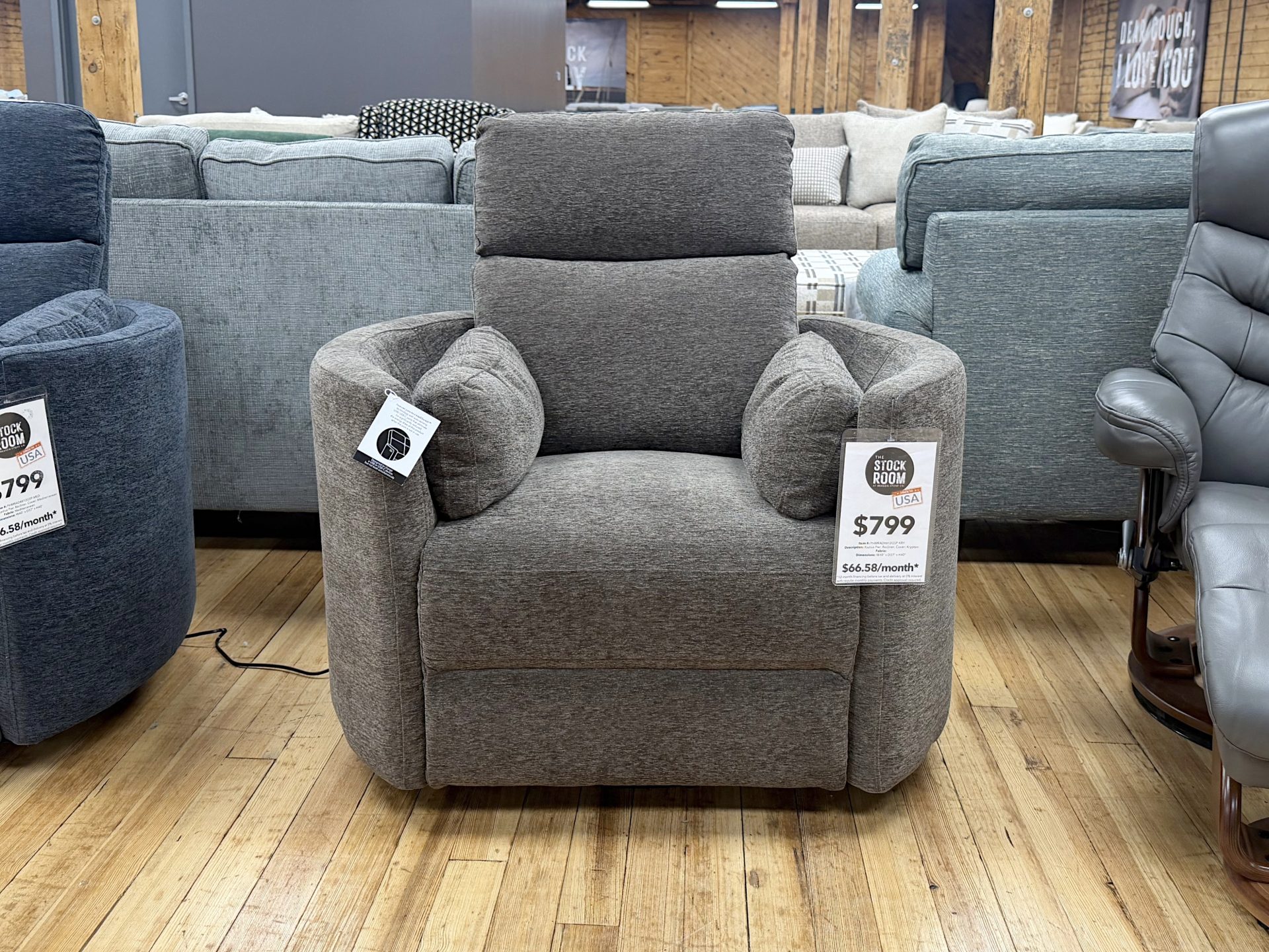 Tezza-2443 Modern charcoal brown textured fabric recliner chair with integrated side bolster pillows, displayed on a light hardwood floor at The Stock Room showroom.