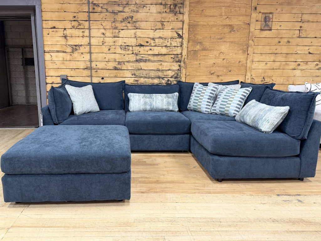 A contemporary navy blue fabric sectional couch with a matching storage ottoman and patterned decorative pillows.