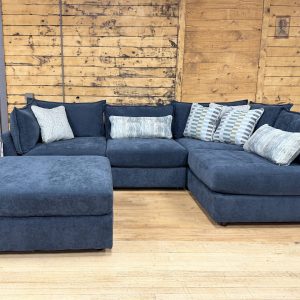 A contemporary navy blue fabric sectional couch with a matching storage ottoman and patterned decorative pillows.