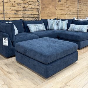 A contemporary navy blue fabric sectional couch with a matching storage ottoman and patterned decorative pillows.