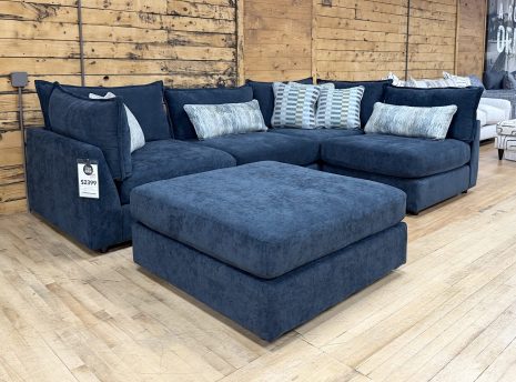 Tezza-5717 A contemporary navy blue fabric sectional couch with a matching storage ottoman and patterned decorative pillows.