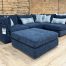 A contemporary navy blue fabric sectional couch with a matching storage ottoman and patterned decorative pillows.