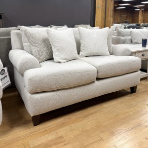 A contemporary light beige upholstered loveseat decorated with textured white and tan accent pillows.