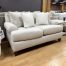 A contemporary light beige upholstered loveseat decorated with textured white and tan accent pillows.
