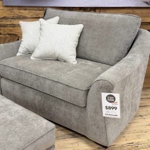 A contemporary oversized taupe fabric lounge armchair decorated with two patterned throw pillows.